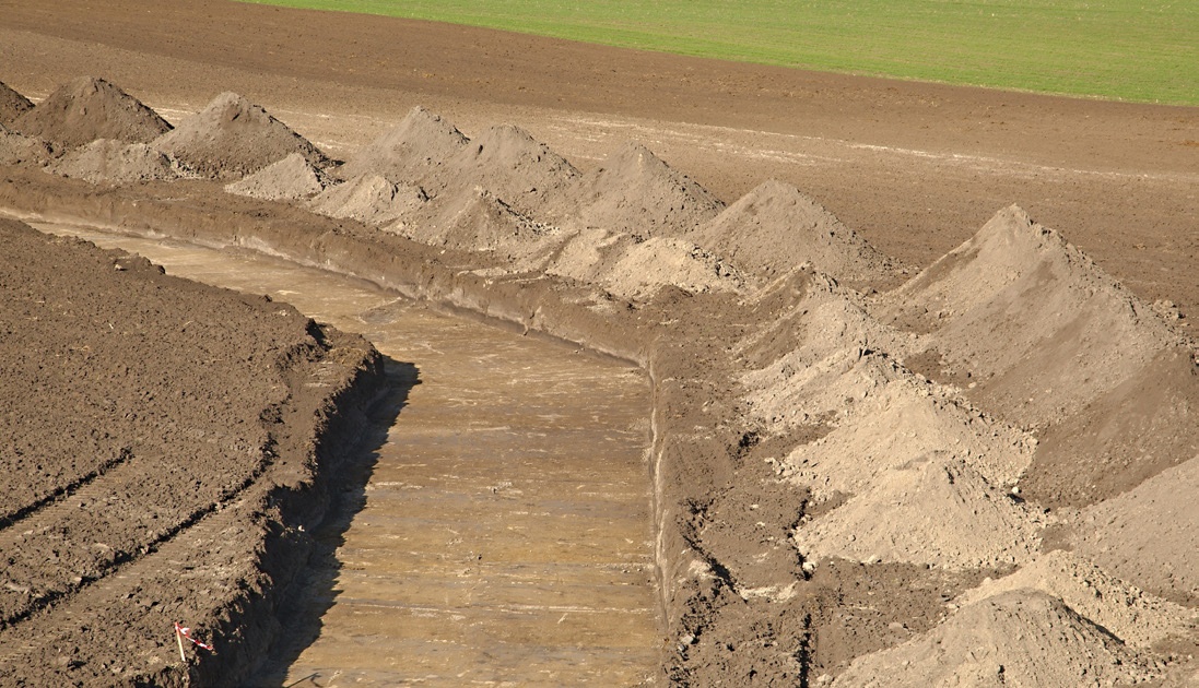 Native soil trench backfill piled alongside an open utility trench