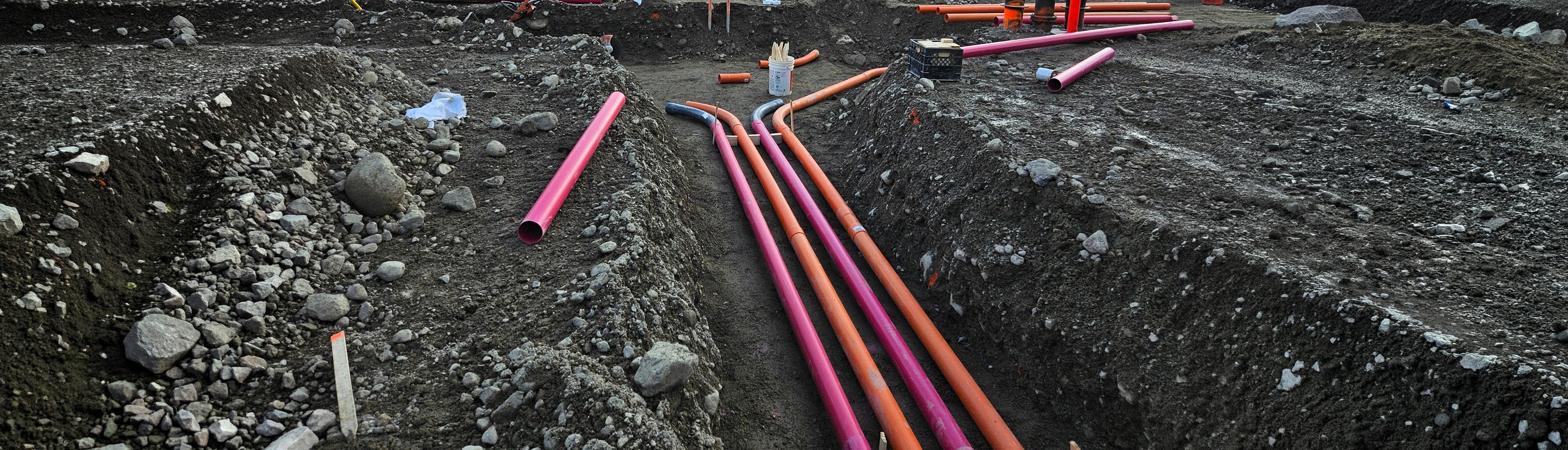Field crew installing orange and red conduits in an open trench for QA/QC verification